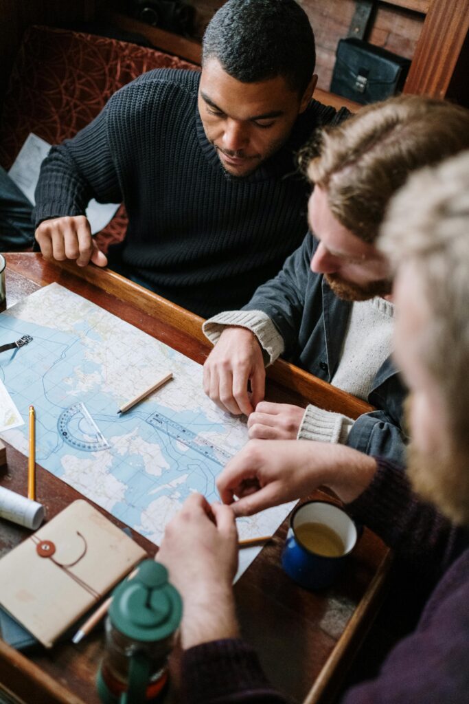 Three men discussing route planning using a maritime map aboard a wooden table.
