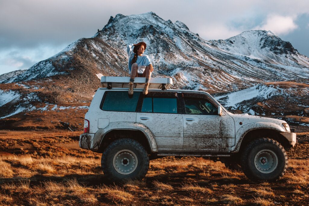 pexels photo 4555454 4555454 Full body woman in casual clothes and hat sitting on offroader rooftop against snowy mountain range in sunny cloudy day